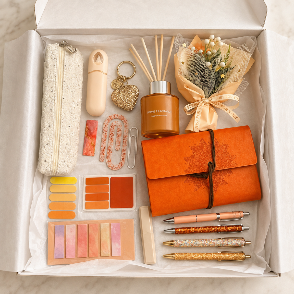 Orange journal and reed diffuser gift box contents in white box including mandala journal, amber diffuser, decorative bouquet, pencil pouch, glitter pens and accessories
