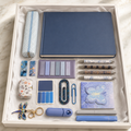 Blue and lavender butterfly stationery gift box in open white box showing slate-blue hardcover notebook, gingham pencil pouch, decorative pens, marble bookmarks, butterfly sticky notes, resin paperclip, dragonfly keychain, correction tape and cactus accessory case