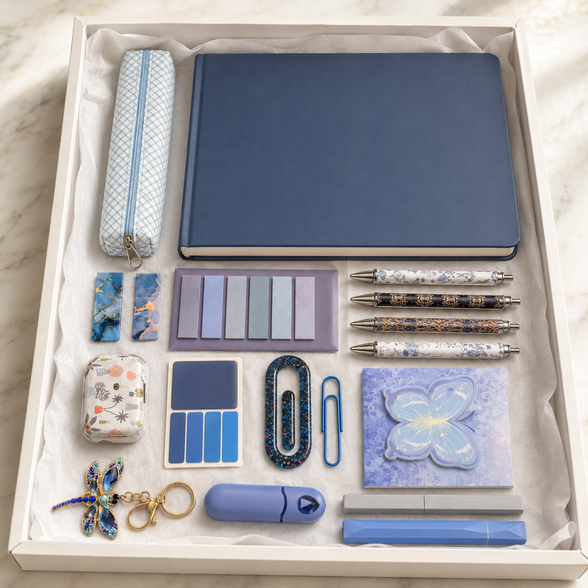 Blue and lavender butterfly stationery gift box in open white box showing slate-blue hardcover notebook, gingham pencil pouch, decorative pens, marble bookmarks, butterfly sticky notes, resin paperclip, dragonfly keychain, correction tape and cactus accessory case
