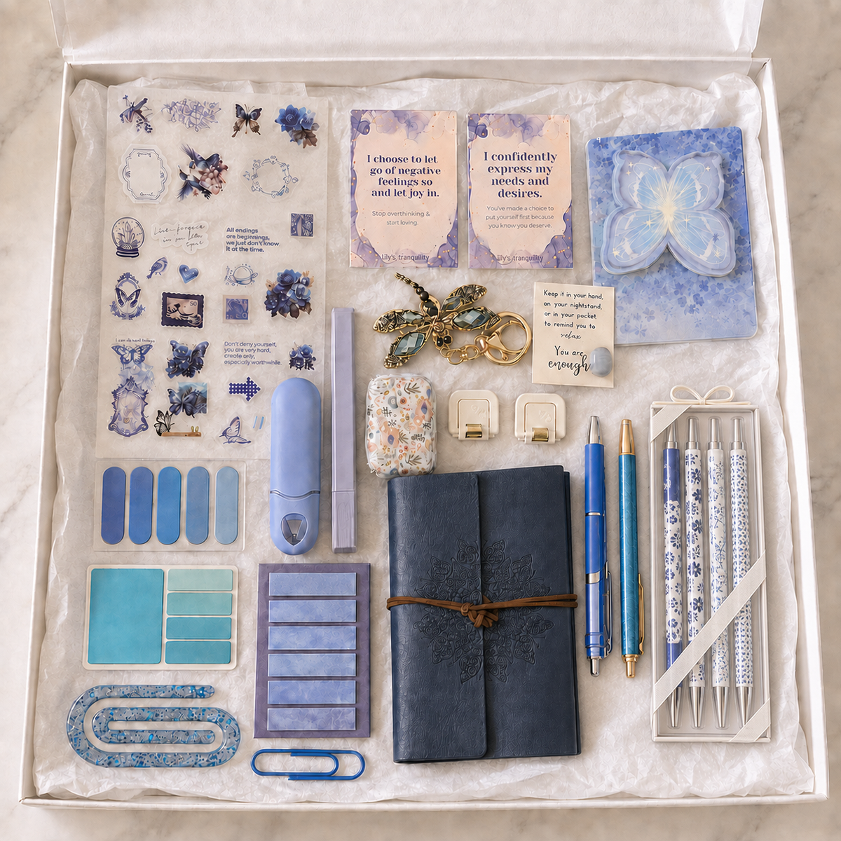 Navy butterfly journal gift box in white box showing embossed mandala wrap journal, boxed blue-and-white pen set, blue retractable pen, blue glitter pen, butterfly sticker sheet, butterfly sticky-note pad, page marker sets, affirmation cards, pocket hug keepsake, dragonfly keychain, lavender correction tape, accessory case, folding utility accessories and blue paperclips