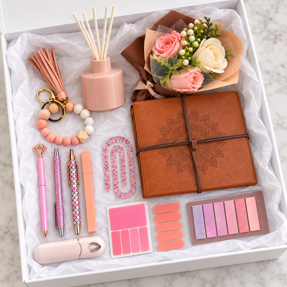 Blush Journal and Diffuser Gift Box – burnt-peach mandala wrap journal, blush reed diffuser, pink and cream rose bouquet, beaded wristlet keychain with tassel, three decorative pens, pink glitter paperclip, correction tape, and sticky note sets arranged in white gift box