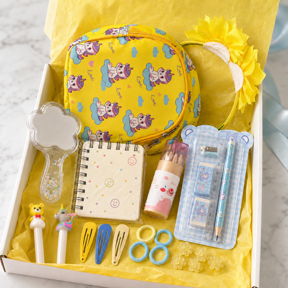 Yellow unicorn gift box in bright yellow tissue paper showing unicorn crossbody bag, flower headband, spiral notebook, mini colored pencils, glitter cloud mirror, light-up character pens, hair clips and hair ties